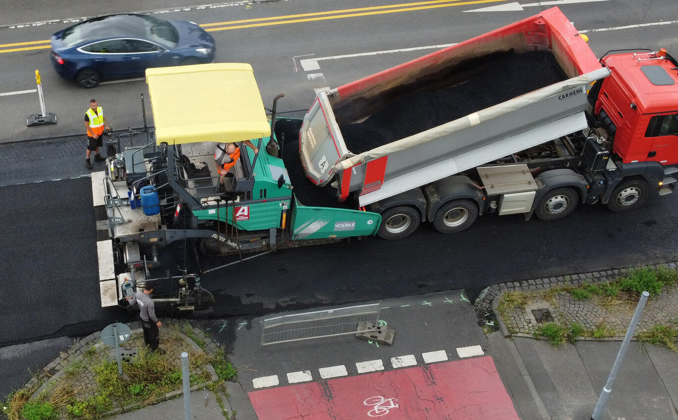 Straßebau: Fertiger bringt frischen Asphalt auf der Straße auf 